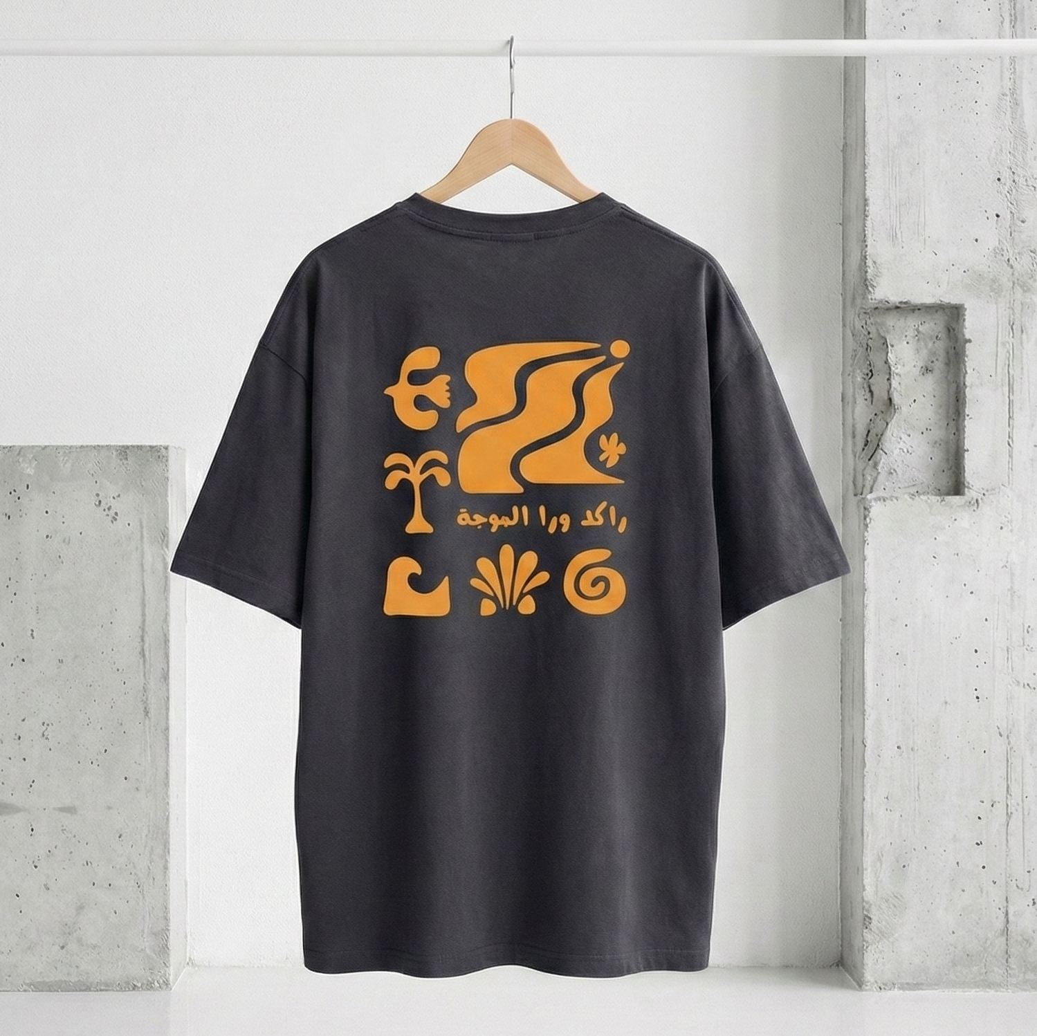 Black t-shirt with orange graphic design on a hanger against a concrete wall.