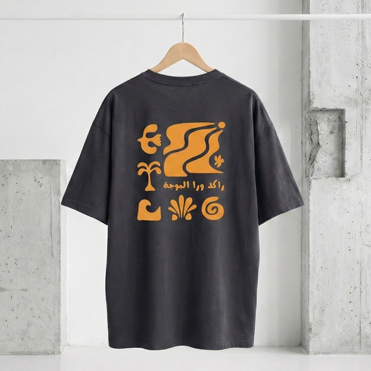 Black t-shirt with orange graphic design on a hanger against a concrete wall.