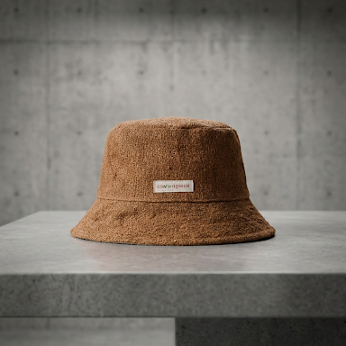 Brown bucket hemp hat with a brand logo on a gray surface and concrete wall background